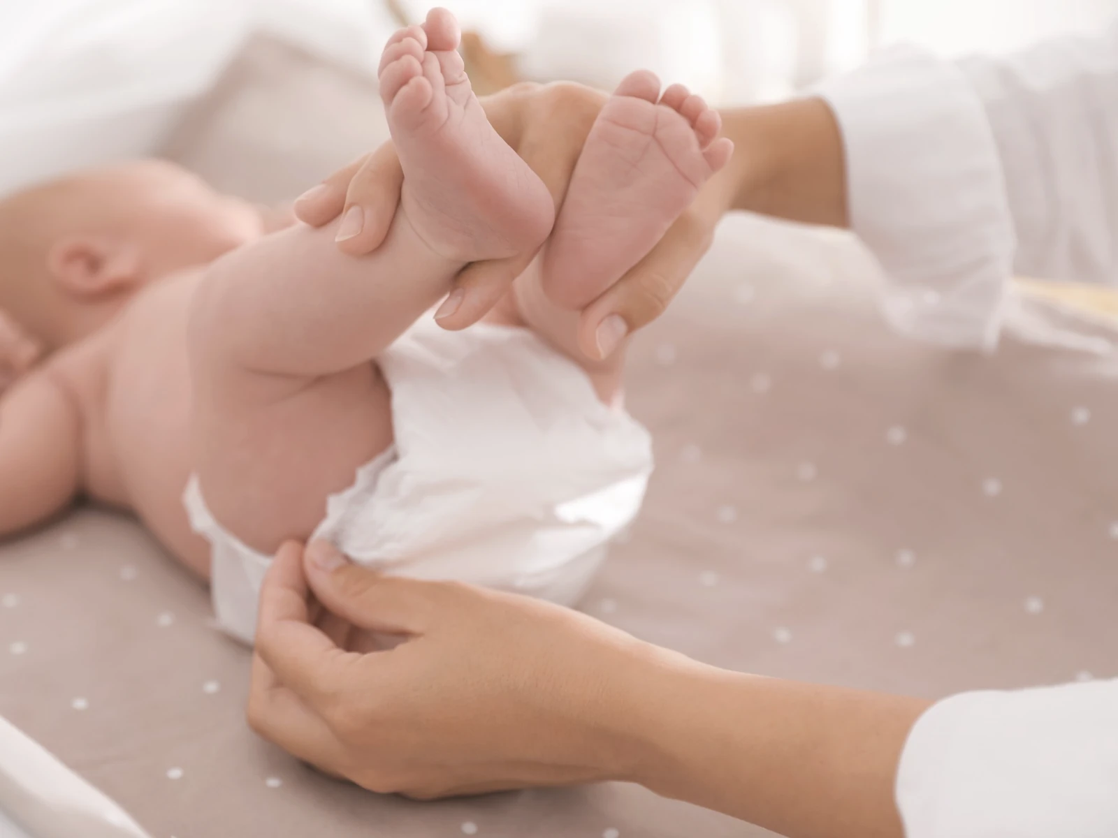 A baby during a gentle diaper change, held with calm and tender hands